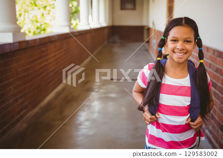 Child student standing in school corridor carrying navy backpack with hair ties, copy space 129583002