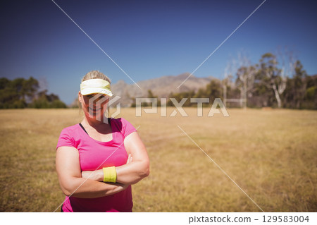 Mid adult woman standing on grassy field wearing pink shirt, yellow visor, wristband near goal post 129583004