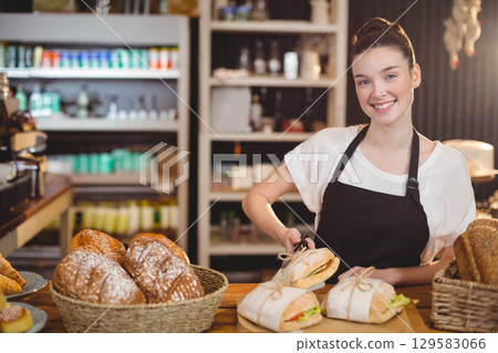 Woman bakery attendant wearing black apron arranging bread loaves in baskets on counter, copy space Woman bakery attendant wearing black apron arranging bread loaves in baskets on counter, copy space 129583066