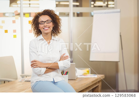 African American woman sitting on wooden desk in modern office reviewing sticky notes with laptop African American woman sitting on wooden desk in modern office reviewing sticky notes with laptop 129583068