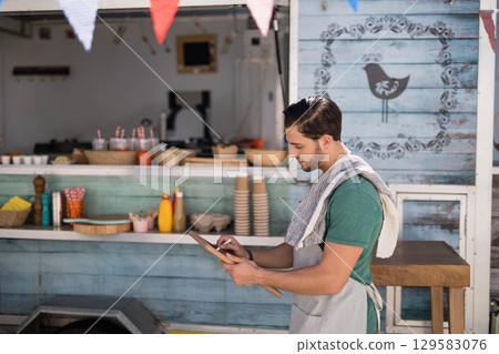 Man wearing green shirt, gray apron arranging paper cups on countertop at food stall, copy space 129583076