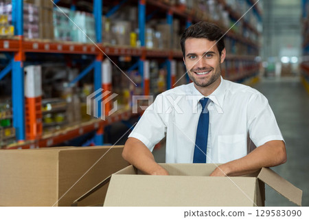 Male supervisor in business attire inspecting cardboard box in warehouse aisle among shelves Male supervisor in business attire inspecting cardboard box in warehouse aisle among shelves 129583090