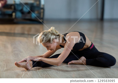 Female yogi in sportswear leaning over leg and grasping foot in fitness studio with gym equipment Female yogi in sportswear leaning over leg and grasping foot in fitness studio with gym equipment 129583095
