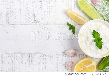 Creamy Greek tzatziki dip served in a bowl with fresh cucumber, garlic, lemon slices, and mint leaves on a rustic wooden table Creamy Greek tzatziki dip served in a bowl with fresh cucumber, garlic, lemon slices, and mint leaves on a rustic wooden table 129583124