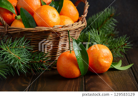 Fresh tangerines in a rustic wicker basket surrounded by pine branches on a wooden table, showcasing vibrant colors and natural textures 129583129