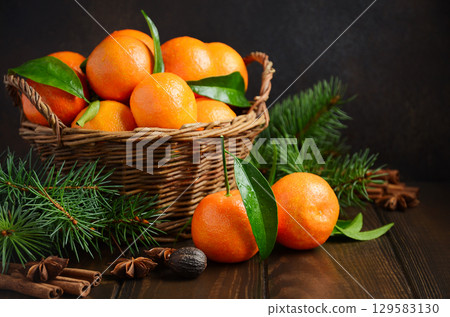 Fresh tangerines in a woven basket surrounded by pine branches and cinnamon sticks, creating a warm and inviting seasonal atmosphere Fresh tangerines in a woven basket surrounded by pine branches and cinnamon sticks, creating a warm and inviting seasonal atmosphere 129583130
