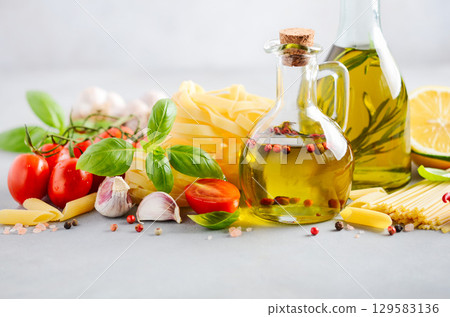 Fresh Italian food ingredients including olive oil, tomatoes, garlic, and pasta arranged beautifully on a light background for culinary inspiration 129583136
