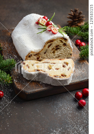 Christmas Stollen bread with powdered sugar, sliced to reveal rich texture, garnished with berries and greenery on rustic wooden board 129583155