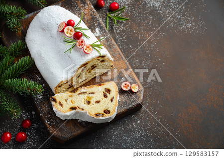 Christmas Stollen bread with powdered sugar, sliced to reveal rich texture and fruit filling, garnished with festive berries and greenery for holiday cheer Christmas Stollen bread with powdered sugar, sliced to reveal rich texture and fruit filling, garnished with festive berries and greenery for holiday cheer 129583157
