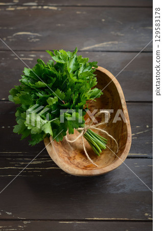 Fresh green parsley bunch placed in a wooden bowl on rustic wooden table, showcasing vibrant colors and natural textures for culinary use 129583178