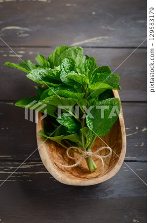 Fresh green mint leaves arranged in a wooden bowl with natural fibers, showcasing vibrant colors and textures for culinary inspiration Fresh green mint leaves arranged in a wooden bowl with natural fibers, showcasing vibrant colors and textures for culinary inspiration 129583179