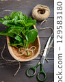 Fresh green mint leaves arranged in a wooden bowl with twine and scissors on a rustic wooden table, showcasing natural ingredients for cooking 129583180