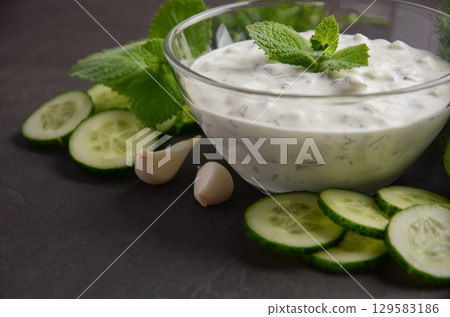Creamy Greek dip sauce tzatziki in a glass bowl garnished with fresh mint leaves, surrounded by sliced cucumbers and garlic cloves, perfect for appetizers Creamy Greek dip sauce tzatziki in a glass bowl garnished with fresh mint leaves, surrounded by sliced cucumbers and garlic cloves, perfect for appetizers 129583186