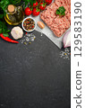 Fresh pork minced meat surrounded by vibrant vegetables, spices, and herbs on a dark stone surface, perfect for culinary creations and recipes 129583190