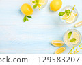 Refreshing lemonade drinks with mint leaves and lemon slices on a light blue wooden table, perfect for summer gatherings and relaxation 129583207