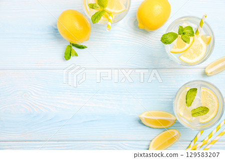 Refreshing lemonade drinks with mint leaves and lemon slices on a light blue wooden table, perfect for summer gatherings and relaxation 129583207