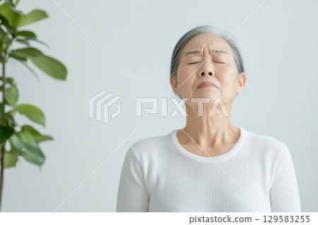 Senior Asian woman performing neck exercises to enhance thyroid health and well-being 129583255