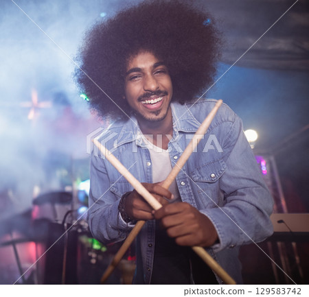 Indian man standing on concert stage holding wooden drumsticks amid colored lights and fog 129583742