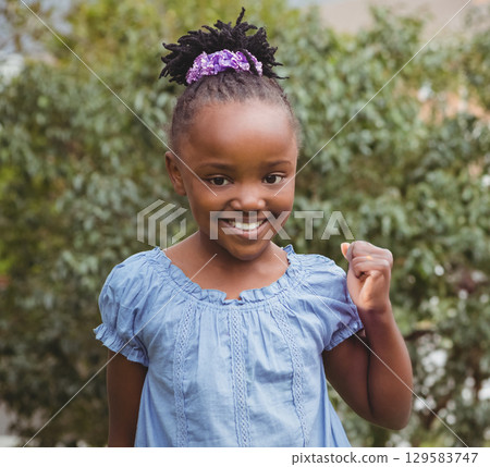 African American female child standing in yard wearing blue dress and purple scrunchie 129583747