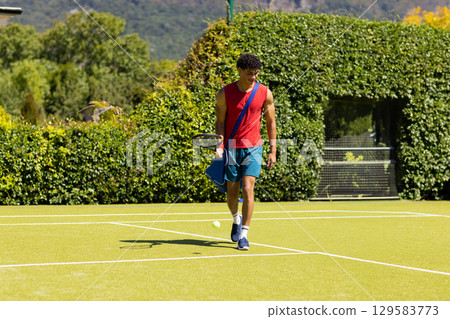 African American male athlete walking on grass tennis court carrying racket bag and tennis ball African American male athlete walking on grass tennis court carrying racket bag and tennis ball 129583773