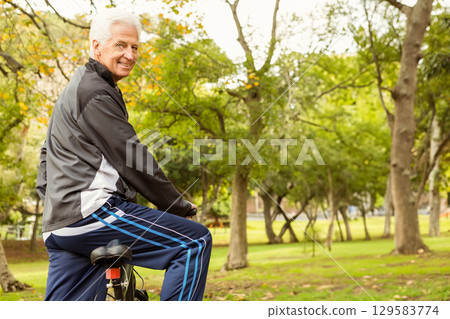 Senior man smiling and riding bicycle through park in zip-up jacket and athletic pants, copy space Senior man smiling and riding bicycle through park in zip-up jacket and athletic pants, copy space 129583774