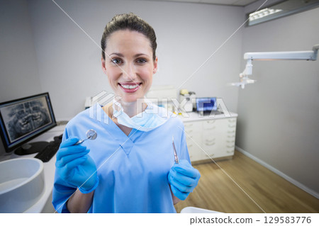 White female dentist holding dental mirror and explorer probe in treatment room with x-ray monitor White female dentist holding dental mirror and explorer probe in treatment room with x-ray monitor 129583776