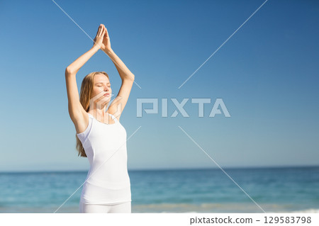 Woman standing on beach wearing white activewear practicing yoga with palms overhead, copy space Woman standing on beach wearing white activewear practicing yoga with palms overhead, copy space 129583798