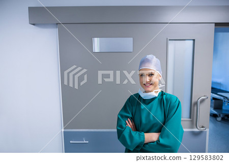 Female surgeon standing in green scrubs by surgical suite door with stretcher visible copy space 129583802