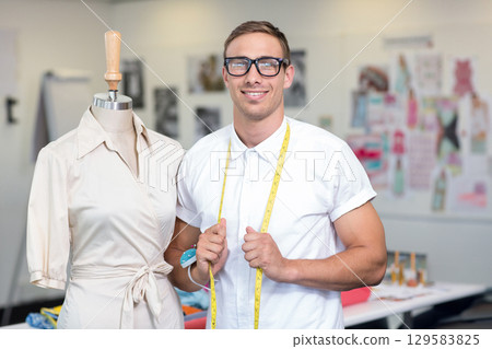 Male designer standing in design studio using measuring tape near wrap dress form, copy space 129583825