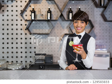 Asian woman bartender holding red lime cocktail behind lounge counter with wine shelves copy space Asian woman bartender holding red lime cocktail behind lounge counter with wine shelves copy space 129583833