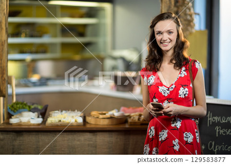 Woman standing at bakery counter and using smartphone in cafe with pastries on display, copy space Woman standing at bakery counter and using smartphone in cafe with pastries on display, copy space 129583877