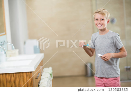 Boy child brushing teeth in home bathroom beside vanity with blue toothbrush and toothpaste tube Boy child brushing teeth in home bathroom beside vanity with blue toothbrush and toothpaste tube 129583885