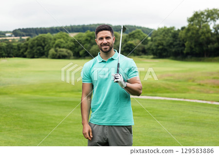 Man in his twenties holding golf club on golf fairway wearing polo shirt with golf glove 129583886