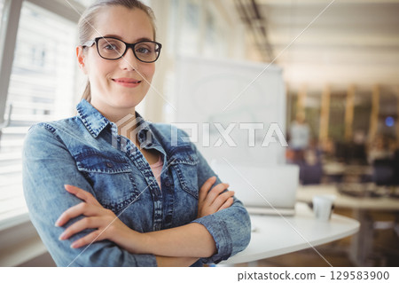 Female professional standing with arms crossed in office near whiteboard and laptop, copy space 129583900