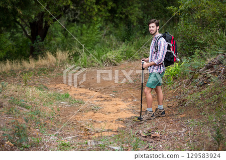 Male hiker standing on forest trail using trekking pole and wearing backpack and boots, copy space 129583924