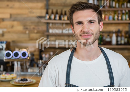 Male bartender wearing denim apron handling beer tap and pastries behind bar, copy space 129583955