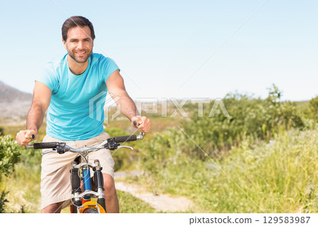 Mid adult male cyclist riding mountain bike with suspension forks along dirt trail in countryside Mid adult male cyclist riding mountain bike with suspension forks along dirt trail in countryside 129583987