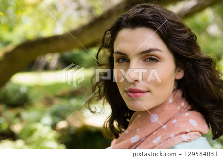Woman standing on right side in garden wearing mint-colored top and polka-dot scarf, copy space 129584031