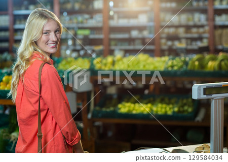 Female shopper in red shirt placing fruits on digital scale in grocery produce section, copy space 129584034