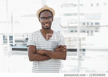 Standing smiling at camera in bright modern interior wearing straw hat and rectangular eyeglasses 129584040