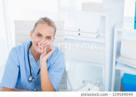 Female doctor in scrubs sitting at desk holding stethoscope and smiling in clinic, copy space Female doctor in scrubs sitting at desk holding stethoscope and smiling in clinic, copy space 129584049
