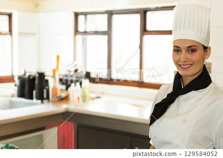 Female chef wearing chef hat standing in professional kitchen near steel countertop, copy space Female chef wearing chef hat standing in professional kitchen near steel countertop, copy space 129584052