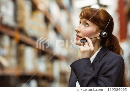 Businesswoman in blazer checking stock with headset in warehouse near racks of boxes, copy space Businesswoman in blazer checking stock with headset in warehouse near racks of boxes, copy space 129584065