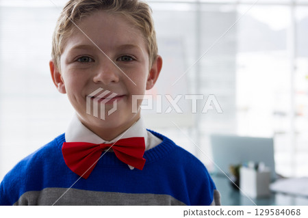 School-age boy standing close to camera in office area, wearing bow tie near whiteboard, copy space School-age boy standing close to camera in office area, wearing bow tie near whiteboard, copy space 129584068