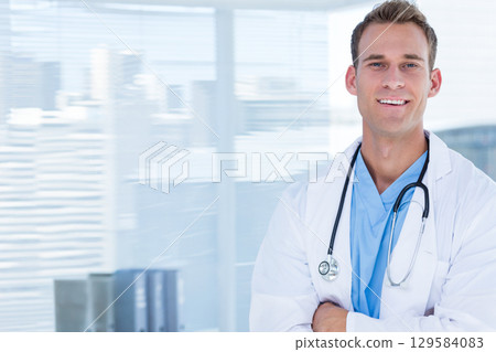 Male doctor standing by clinic window in scrubs and coat holding stethoscope by binders, copy space 129584083
