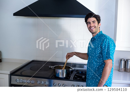 Man stirring meal on stainless steel stove in home kitchen with wooden spoon, copy space 129584110