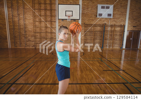 Female athlete in sportswear holding basketball and practicing jump shot on court under backboard Female athlete in sportswear holding basketball and practicing jump shot on court under backboard 129584114