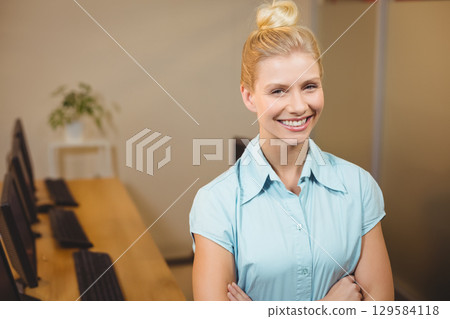 Woman wearing light blue shirt standing in computer lab by desktop monitors and potted plant 129584118