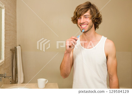 Mid adult man standing at home bathroom brushing teeth with toothbrush under chrome faucet by sink Mid adult man standing at home bathroom brushing teeth with toothbrush under chrome faucet by sink 129584129