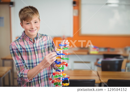 School-age boy smiling and assembling colorful plastic DNA model at classroom desk, copy space School-age boy smiling and assembling colorful plastic DNA model at classroom desk, copy space 129584152